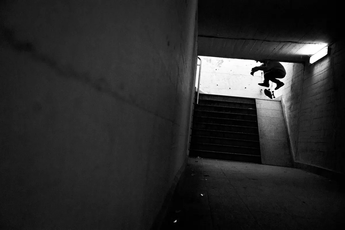 Nollie flip in a dark underpass, against the light from the stairs behind